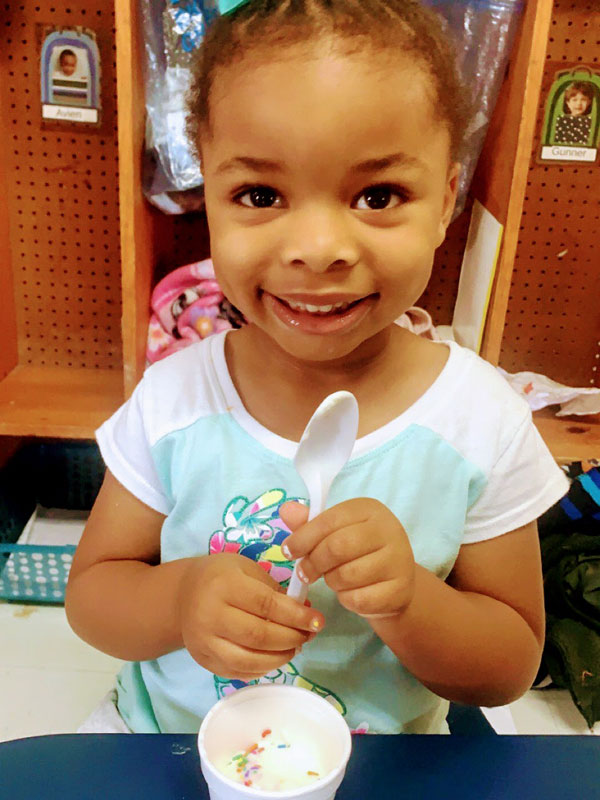 Smiling child with ice cream and a spoon.