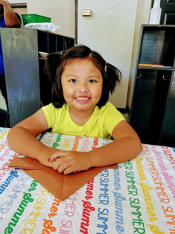 Smiling girl at table with folded paper.