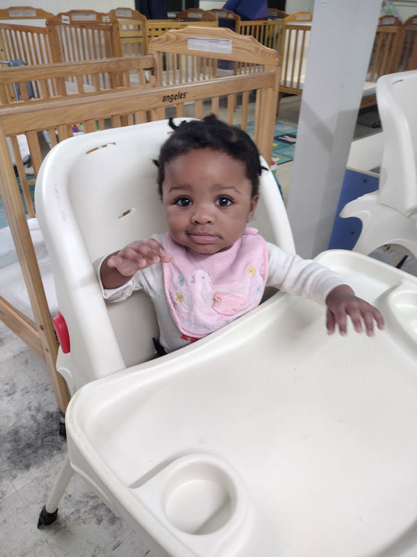 Baby in a high chair reaching out.