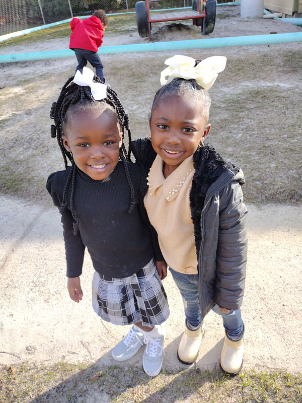 Two smiling girls with hair bows outside.