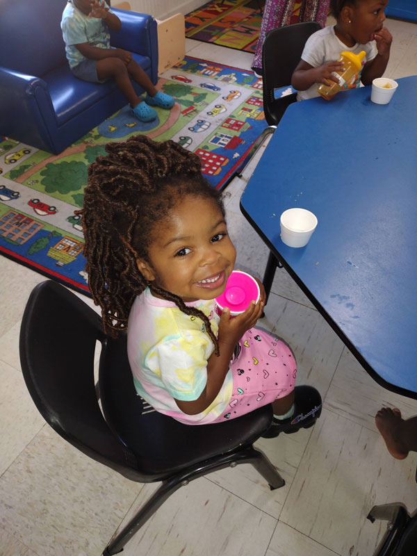 Child in a chair holding a pink toy cup.