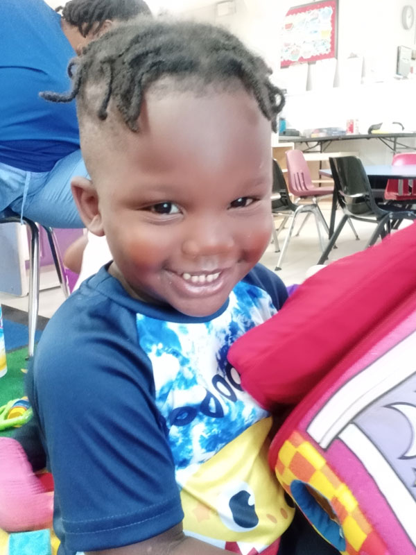 Boy with a tie-dye shirt smiling in a classroom.