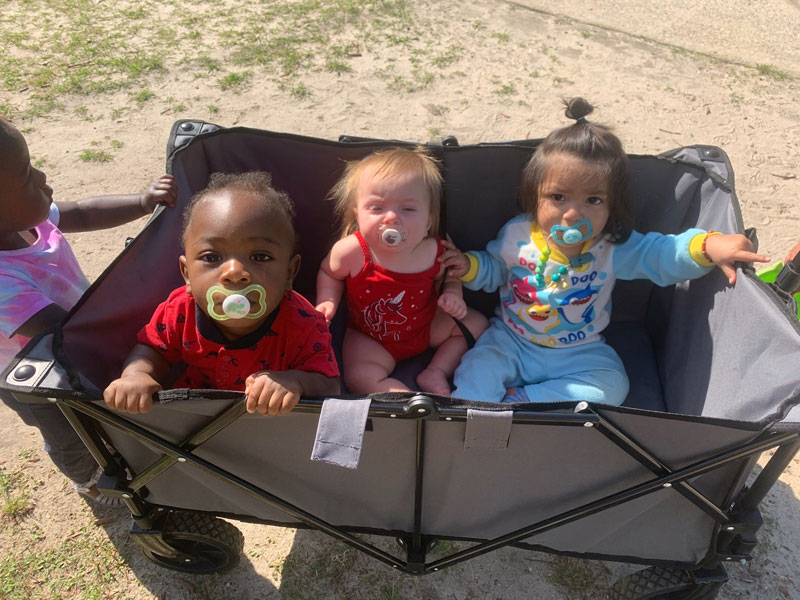 Three toddlers with pacifiers in a stroller.