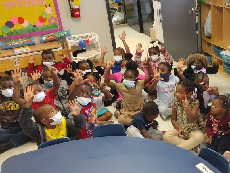 Group of children raising hands at a table.