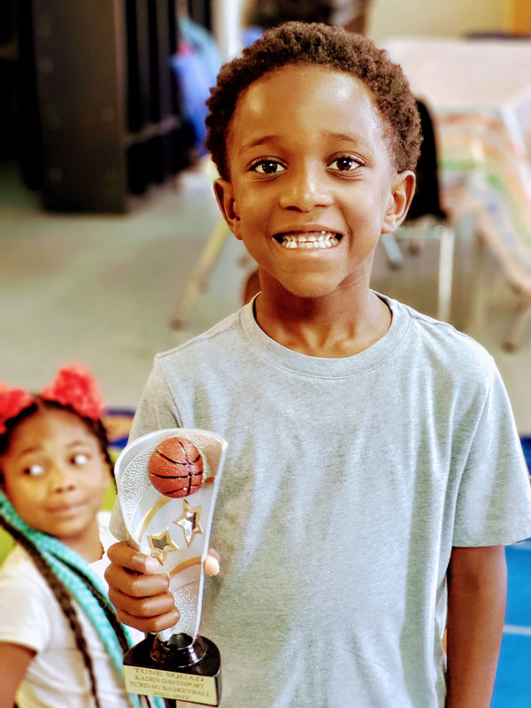 Boy proudly holding a basketball trophy with a smile.