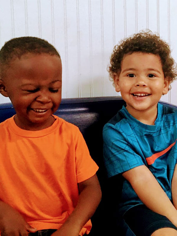 Two children laughing together on a blue bench.