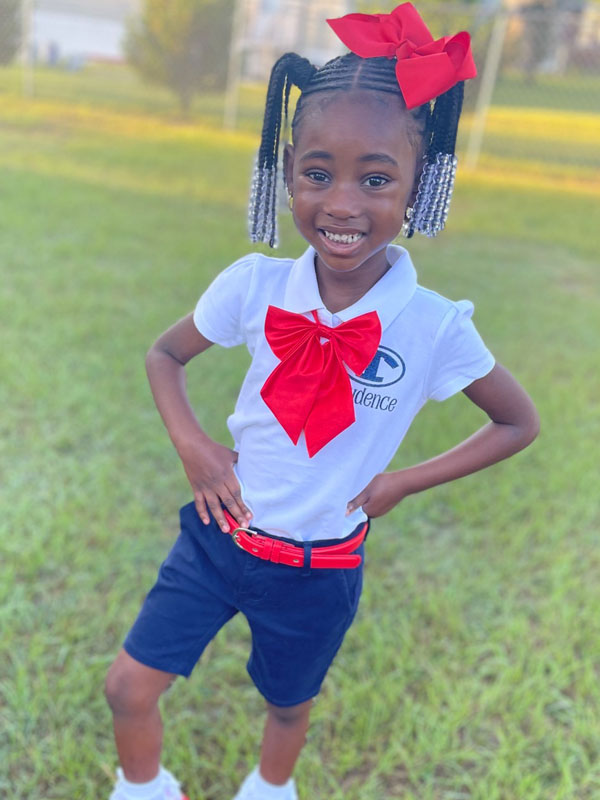 Smiling girl posing with hands on hips, wearing a school uniform.