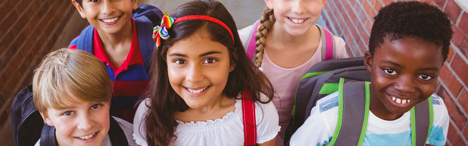 Children with backpacks smiling at school entrance.